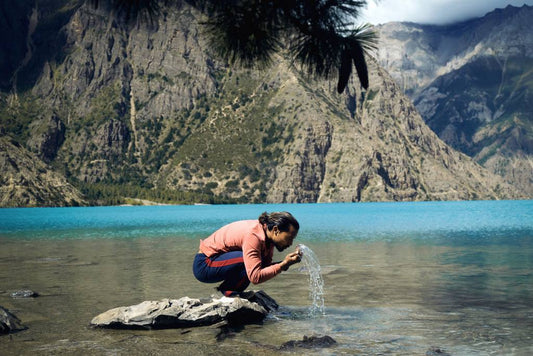 Ein hockender Mann am See, der sich das Gesicht mit dem Seewasser wäscht. Seifenrest auf der Haut